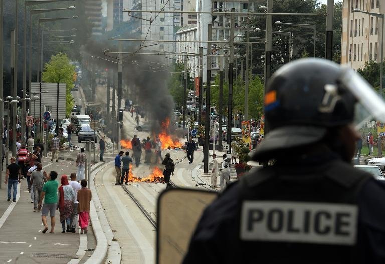 A French riot police officer looks at burning barricades along the tramway line in Sarcelles, a suburb north of Paris, on July 20, 2014. (AFP Photo/Pierre Andrieu)
